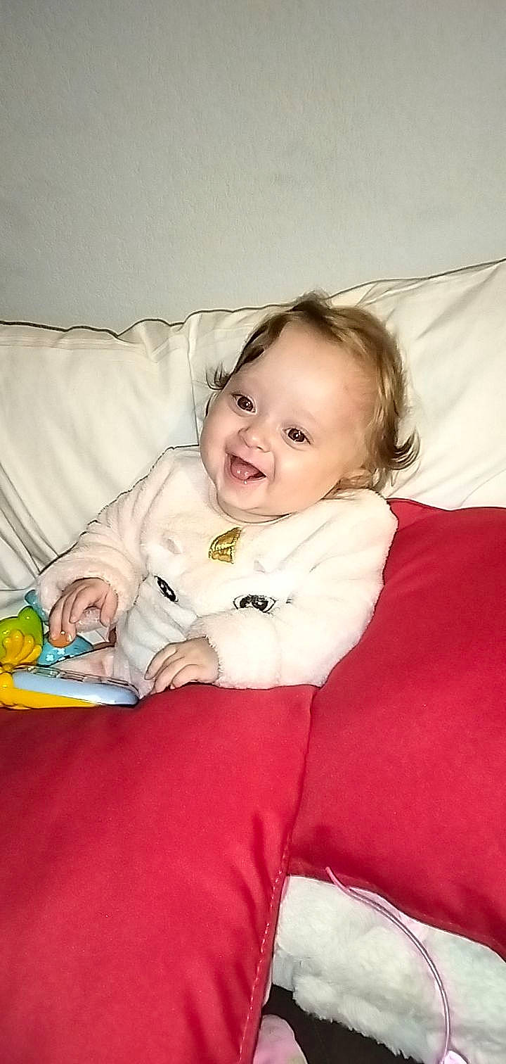 Melyana participe au concours pour gagner de l'argent avec cette photo : baby, baby_toddler_clothing, cheek, comfort, couch, event, eye, face, fun, hand, happy, head, iris, joy, linens, person, room, sitting, skin, sleeve