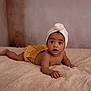 baby, infant, child, blanket, bedroom, turban, headwear, polka_dot, yellow_shorts, skin, cute, expression, lying_down, indoors, portrait, soft_texture, young, looking, hand, face