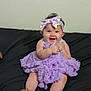 adult_hand, baby, black_background, child, curly_hair, cute, dress, feet, hands, happy, headband, indoor, infant, person, portrait, purple, sitting, smiling, support, thumbs_up