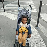 Rodady participe au concours pour gagner de l'argent avec cette photo : toddler, child, stroller, puffer_jacket, boots, sidewalk, urban, crosswalk, pedestrian, bicycle, street, city, outerwear, winter_clothing, curb, metal_pole, asphalt, baby, portrait, outdoor