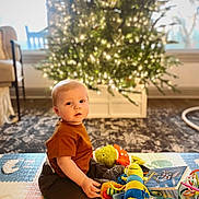 Sawyer joined the competition — help win amazing prizes! baby, child, indoor, play_mat, plush_toy, book, christmas_tree, holiday, decorations, carpet, window, chair, person, sitting, soft_light, toy, cute, floor, home, young_child