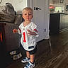 Sawyer joined the competition — help win amazing prizes! child, toddler, boy, football_jersey, sportswear, number_one, standing, indoors, portrait, serious_expression, blond_hair, blue_sneakers, white_jersey, wooden_floor, couch, dog_bowl, living_room, kitchen, open_door, flowers