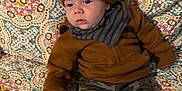 Bryson joined the competition — help win amazing prizes! baby, blanket, brown_clothing, camo_pants, child, cozy, cute, expression, face, hat, headwear, indoor, infant, jacket, patterned_blanket, person, seated, socks, warm_clothing, young_child