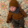 Bryson joined the competition — help win amazing prizes! baby, blanket, brown_clothing, camo_pants, child, cozy, cute, expression, face, hat, headwear, indoor, infant, jacket, patterned_blanket, person, seated, socks, warm_clothing, young_child