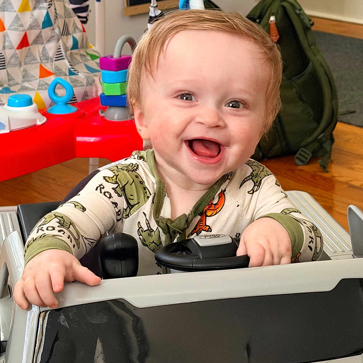 Björn joined the competition — help win amazing prizes! toddler, child, smile, happy, toy_car, indoor, dinosaur_onesie, baby, face, hands, play, joy, backpack, wooden_floor, colorful_toys, steering_wheel, cute, portrait, person, home