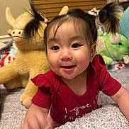 Kaia joined the competition — help win amazing prizes! baby, child, smile, pigtails, red_shirt, plush_toy, stuffed_animal, bedroom, blanket, indoor, happy, cute, infant, person, portrait, toy, childhood, face, young, home