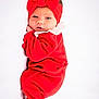 baby, newborn, infant, red_clothing, headband, bow, lying_down, white_background, soft_texture, cute, portrait, child, face, eyes, hand, sleepwear, indoors, cozy, small_person, adorable