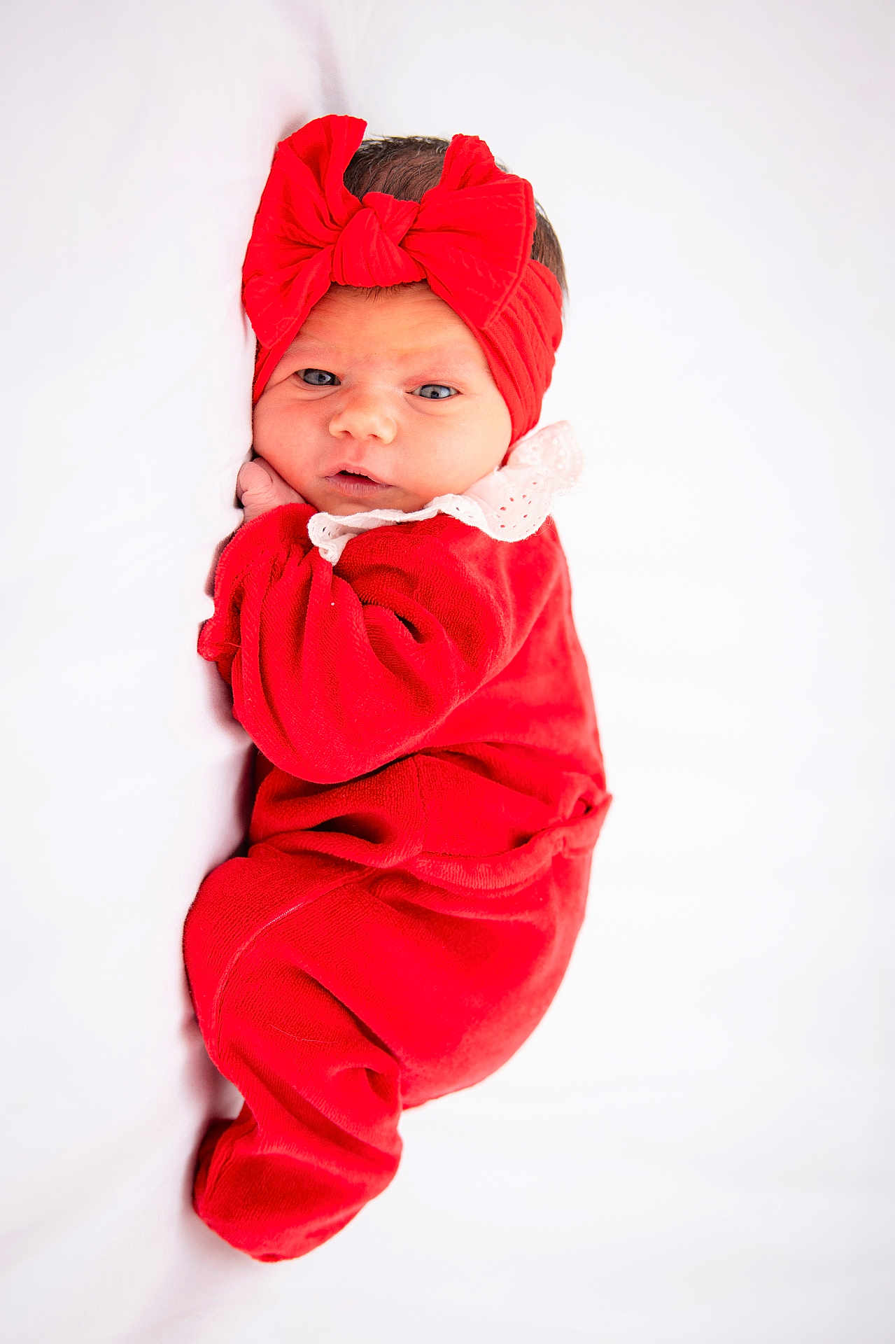 Kinsley participe au concours pour gagner de l'argent avec cette photo : baby, newborn, infant, red_clothing, headband, bow, lying_down, white_background, soft_texture, cute, portrait, child, face, eyes, hand, sleepwear, indoors, cozy, small_person, adorable