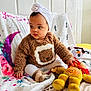baby, bed, bedroom, blanket, clothing, cushion, face, furniture, happy, hat, head, homedecor, indoors, person, photography, portrait, quilt, sitting, smile, toy