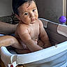 baby, child, infant, bath, bathtub, bath_seat, water, wet, purple_toy, serious_expression, dark_hair, sitting, portrait, indoor, home, adult_arm, support, bathroom, closeup, safe_bathing