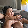 baby, child, infant, bathtub, bath, water, smiling, wet, adult, parent, caregiver, bathroom, yellow_curtain, toy_cup, portrait, sitting, happy, indoor, family, hygiene