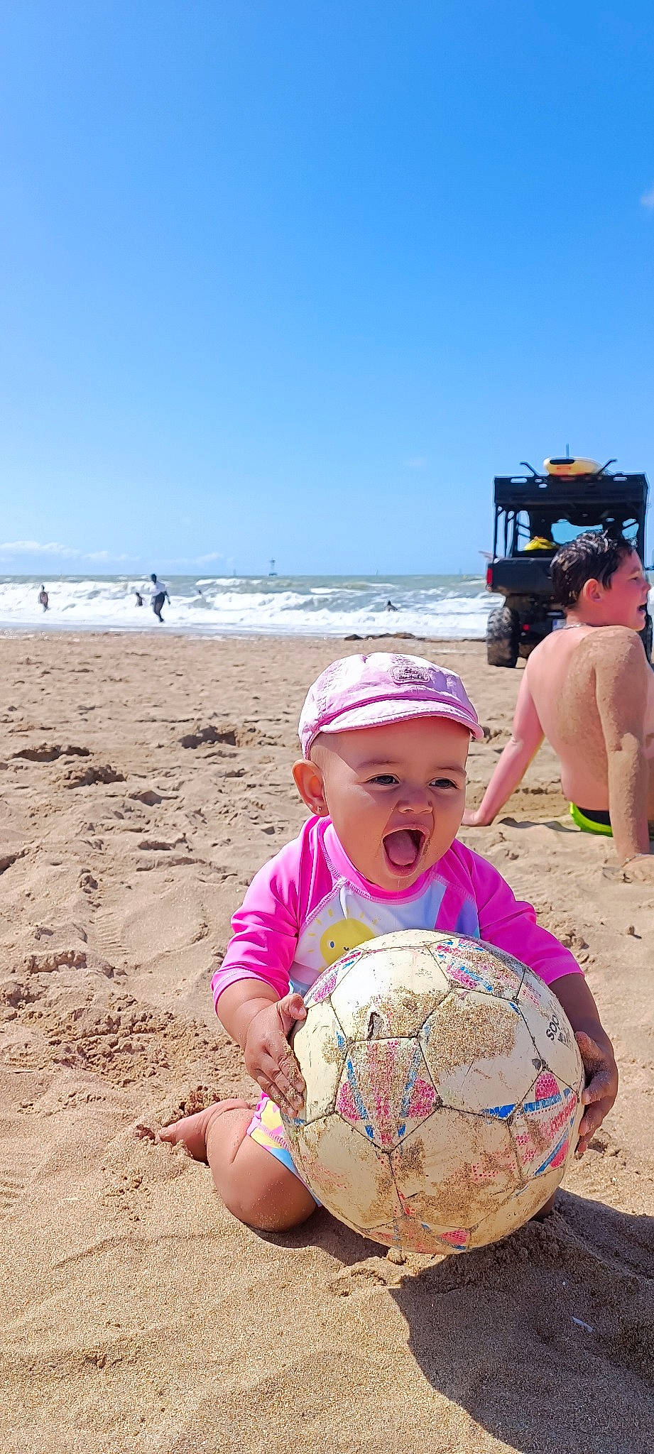 Juanita a rejoint le concours — aidez-le/la à gagner de superbes lots ! ball, beach, body_of_water, football, fun, happy, hat, headwear, leisure, people_in_nature, people_on_beach, person, sand, shorts, sky, soccer, sports_equipment, sports_toy, summer, toddler
