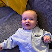 Timothé a rejoint le concours — aidez-le/la à gagner de superbes lots ! baby, child, clothing, comfort, couch, cozy, face, gray_couch, happy, indoors, infant, person, pillow, portrait, relaxing, sitting, smiling, sweatshirt, yellow_pillow, young_child