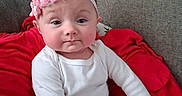 Peyton is registered to the contest to win money with this photo: baby, infant, child, headband, pink, flower, red_blanket, couch, plaid_pants, white_shirt, indoors, portrait, cute, expression, sitting, person, young_child, cozy, soft_lighting, casual