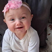 Peyton is registered to the contest to win money with this photo: baby, infant, headband, pink, white_clothing, smile, face, cushion, indoors, child, cute, portrait, sitting, apparel, young_child, human, skin, expression, cheerful, cozy