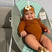 Nicole is registered to the contest to win money with this photo: baby, infant, smiling, headband, flower, baby_seat, clothing, orange, cute, indoors, face, person, furniture, sitting, legs, hand, comfortable, happy, closeup, soft