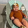 baby, infant, smiling, headband, flower, baby_seat, clothing, orange, cute, indoors, face, person, furniture, sitting, legs, hand, comfortable, happy, closeup, soft