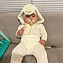 Nicole is registered to the contest to win money with this photo: baby, infant, pacifier, white_clothing, knitwear, hood, flower_headband, sitting, couch, indoor, child, cute, portrait, furniture, sock, hand, face, looking_at_camera, home, soft_lighting