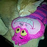 cat, orange_cat, sleeping, plush_toy, pink, purple, yellow_eyes, stuffed_animal, cozy, nap, feline, pet, soft_texture, cute, indoors, resting, animal, closeup, adorable, comfort