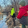 child, adult, fishing, creek, riverbank, rock, winter_clothing, knit_hat, jacket, boots, trees, leafless_trees, outdoor, nature, water, fishing_rod, person, daylight, recreation, forest