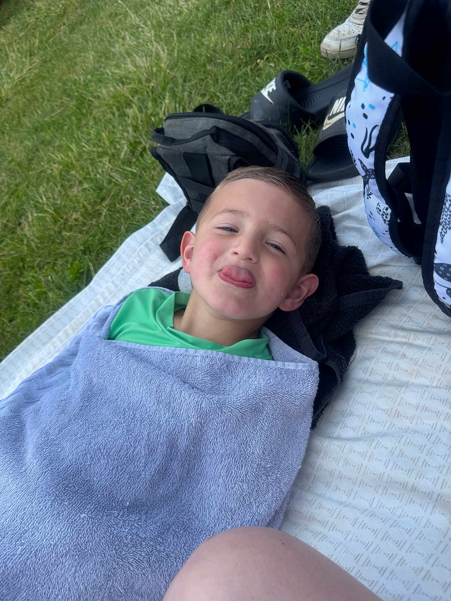 Colson joined the competition — help win amazing prizes! child, towel, grass, backpack, shoes, blanket, outdoor, playful, smiling, tongue_out, person, casual, relaxed, picnic, green, young, recreation, resting, fun, happy