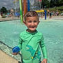 child, boy, swimwear, pool, water, splash_pad, toy, smile, outdoor, summer, recreation, play, water_spray, green_shirt, dinosaur, park, people, sunny, fun, happy