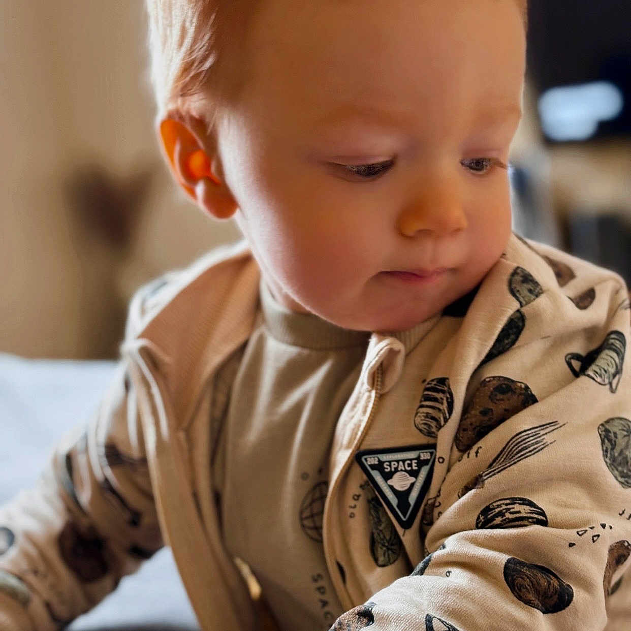 Owen a rejoint le concours — aidez-le/la à gagner de superbes lots ! baby, beige_clothing, candid, casual_wear, child, close_up, curious, cute, face, hand, indoor, long_sleeves, portrait, red_hair, sitting, soft_light, space_print, toddler, warm_tones, young_child