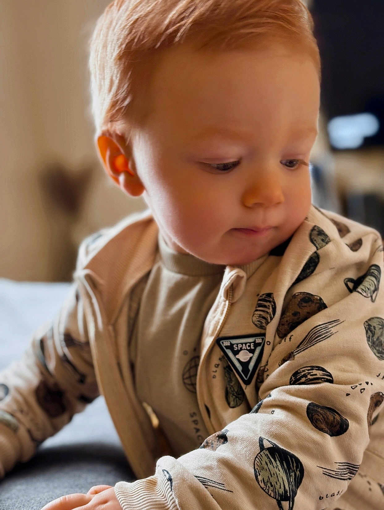 Owen a rejoint le concours — aidez-le/la à gagner de superbes lots ! toddler, child, red_hair, curious, beige_clothing, space_print, long_sleeves, indoor, soft_light, portrait, close_up, young_child, candid, casual_wear, baby, face, hand, sitting, warm_tones, cute