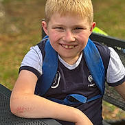 Timéo a rejoint le concours — aidez-le/la à gagner de superbes lots ! backpack, blond_hair, boy, casual, child, daylight, face, grass, happy, metal, nature, outdoor, person, portrait, resting, seat, short_sleeve_shirt, smiling, table, young