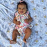 baby, child, smiling, happy, infant, blanket, pattern, animal_print, floral_outfit, pink_bow, lying_down, cute, portrait, skin, hand, foot, indoors, soft_texture, colorful, person