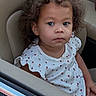 child, toddler, car_seat, curly_hair, white_dress, ladybug_print, portrait, indoor, seat, car, person, cute, young_child, expressionless, skin, face, sitting, clothing, hair, young
