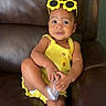 toddler, child, yellow_clothing, sunglasses, flower_shaped, leather_couch, indoor, cute, playful, footwear, baby, smiling, portrait, small_child, casual, fashion, seat, happy, one_person, relaxed