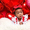 baby, child, infant, red_bow, headband, heart_pattern, white_outfit, fluffy_blanket, red_balloons, pink_balloon, valentines_day, cute, portrait, smiling, indoor, celebration, holiday, decorations, person, closeup