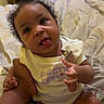 Delilah is registered to the contest to win money with this photo: baby, child, onesie, tongue_out, bed, hand, person, indoor, dresser, clothing, cute, expression, skin, hair, earrings, holding, sitting, infant, room, casual