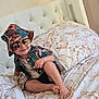 barefoot, bed, bedding, bracelet, bucket_hat, child, cute, fashion, hat, headwear, indoor, patterned_clothing, person, pillow, portrait, relaxed, shirt, smile, sunglasses, toddler