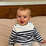 Noé participe au concours pour gagner de l'argent avec cette photo : baby, bed, child, clothing, cute, eyes, face, hand, happy, indoor, infant, mouth, pants, person, portrait, sitting, skin, smiling, striped_sweater, wooden_headboard