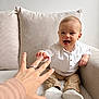adult_hand, baby, beige_pants, blanket, child, couch, cozy, curious, furniture, hand, happy, indoor, interaction, pillow, portrait, reaching, ring, smiling, white_shirt, white_shoes