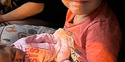 Ellianna is registered to the contest to win money with this photo: child, baby, smile, sleeping, pink_clothing, pajamas, holding, blanket, patterned_blanket, indoor, person, family, sibling, happy, young_child, infant, portrait, face, warm_light, cozy