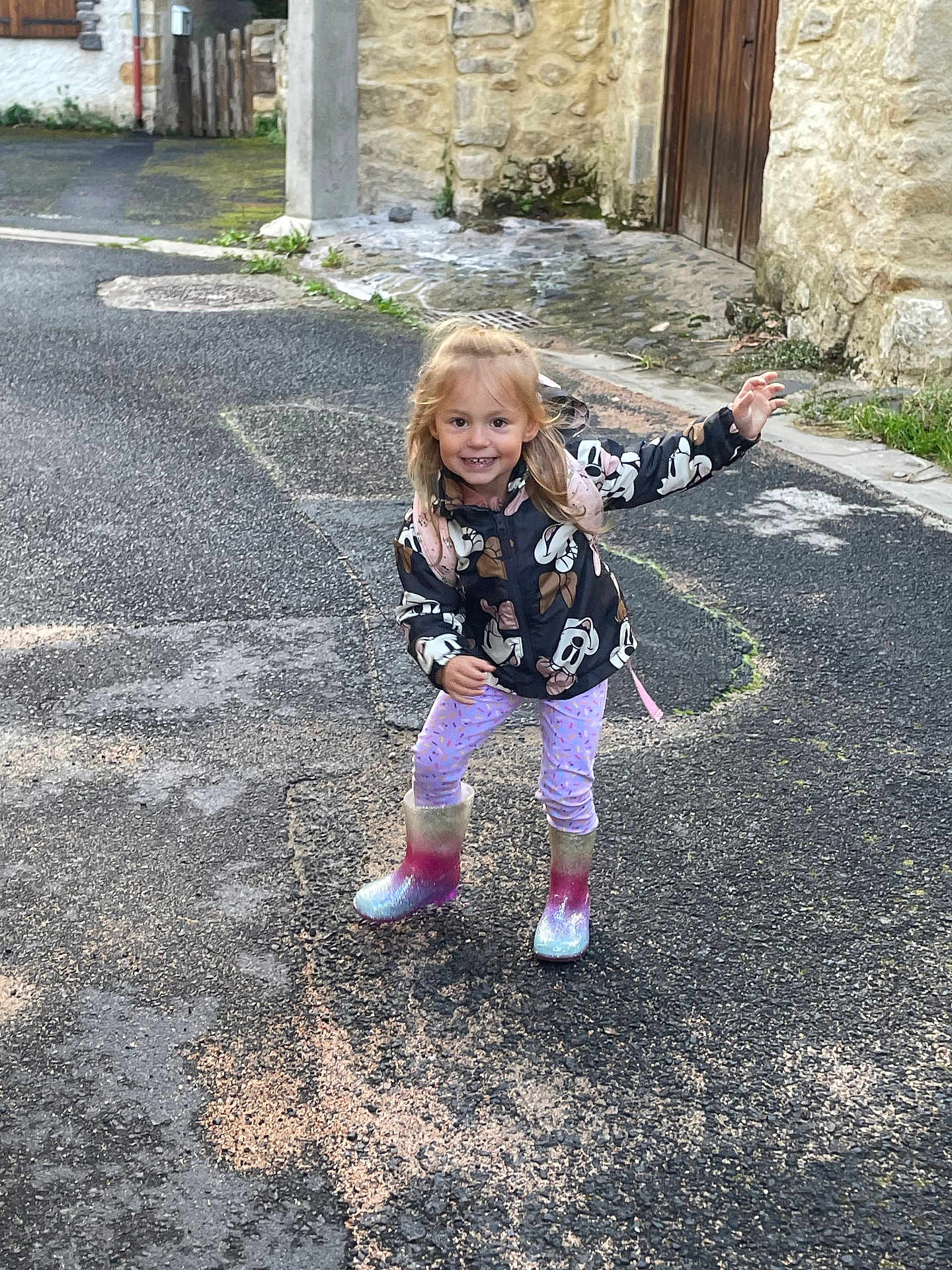 Eva participe au concours pour gagner de l'argent avec cette photo : child, girl, rain_boots, jacket, mickey_mouse, playful, hopscotch, chalk, street, pavement, stone_wall, door, outdoor, smiling, blonde_hair, casual_clothing, playtime, urban, young_child, happy