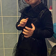 Eva a rejoint le concours — aidez-le/la à gagner de superbes lots ! child, smiling, costume, black_clothing, veil, red_flowers, bathroom, tiles, playful, portrait, indoor, person, happy, young, dressed_up, hand_gesture, headwear, floor_tiles, curtain, household