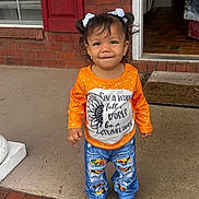Malani joined the competition — help win amazing prizes! child, toddler, girl, standing, pigtails, white_bows, orange_shirt, sunflower, jeans, ripped_jeans, brown_shoes, porch, brick_wall, red_shutter, doorway, concrete_floor, smiling, cute, outdoor, casual_clothing