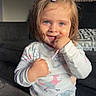 child, girl, toddler, portrait, smiling, happy, standing, pajamas, blonde_hair, hair_clip, blue_eyes, indoors, living_room, sofa, cushion, sunlight, natural_light, casual, playful, animal_print