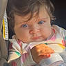 baby, infant, child, car_seat, portrait, face, blue_eyes, brown_hair, looking_at_camera, sitting, toy, bottle, blanket, colorful_clothing, onesie, indoor, vehicle, sunlight, close_up, safe
