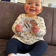 Adèle participe au concours pour gagner de l'argent avec cette photo : baby, blue_eyes, child, clothing, couch, hands, happy, headband, indoor, infant, milestone_card, person, portrait, rosy_cheeks, sitting, smiling, socks, sofa, teddy, teeth