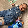 baby, infant, denim_overalls, smiley_face_pattern, plush_toy, stitch_character, milestone_card, mickey_mouse, blanket, soft_texture, cute, lying_down, happy, child, young, playful, indoor, clothing, portrait, adorable