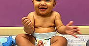 Ryan joined the competition — help win amazing prizes! baby, child, smiling, diaper, sitting, plush_toy, purple_wall, paper_sheet, happy, cute, indoor, playtime, feet, hands, curly_hair, expression, toy, colorful, infant, room
