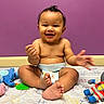 baby, child, smiling, diaper, sitting, plush_toy, purple_wall, paper_sheet, happy, cute, indoor, playtime, feet, hands, curly_hair, expression, toy, colorful, infant, room