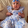 baby, child, blue_bow, dress, headband, sitting, couch, curious, indoors, foot, cute, portrait, person, furniture, fabric, pattern, smiling, happy, skin, young