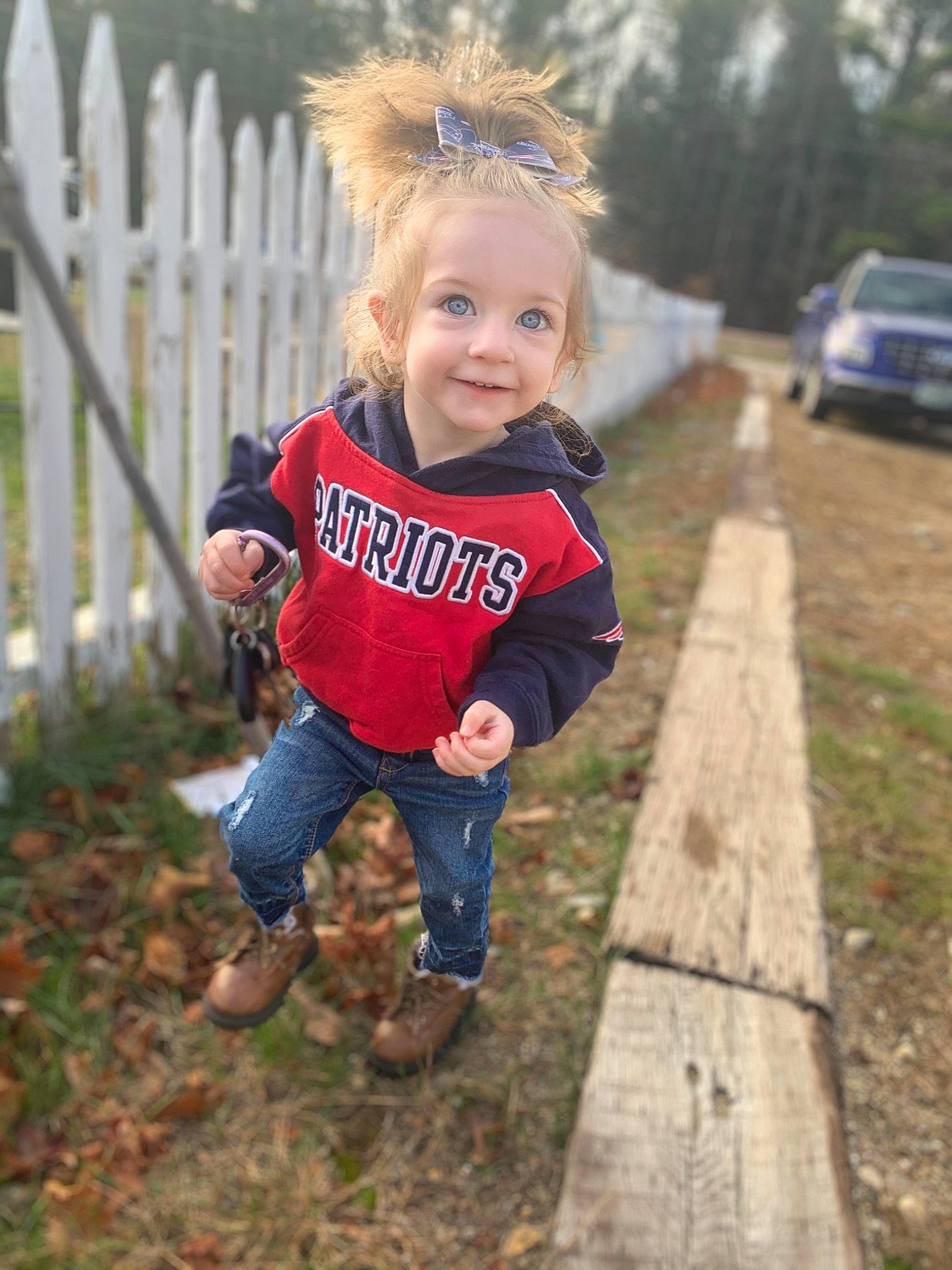 Ellianna is registered to the contest to win money with this photo: baby_toddler_clothing, blond, boot, child, child_model, city_car, denim, family_car, fence, full_size_car, hair_accessory, home_fencing, jeans, joy, mammal, mid_size_car, person, picket_fence, toddler, vehicle_registration_plate