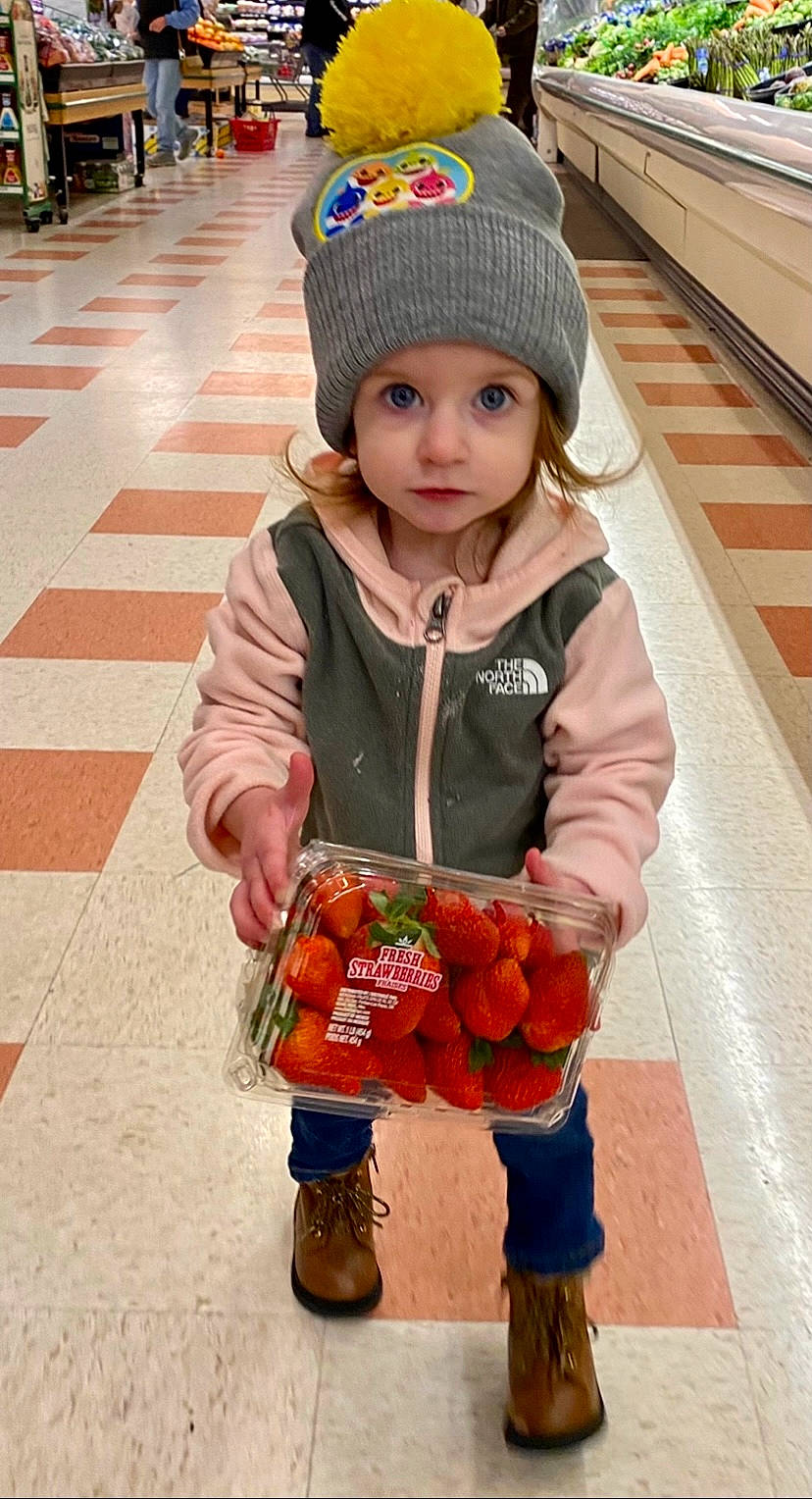 Ellianna joined the competition — help win amazing prizes! beanie, cap, child, city, fashion_accessory, flooring, food, fruit, green, headwear, hoodie, knit_cap, natural_foods, orange, person, photograph, recreation, red, sitting, street_fashion